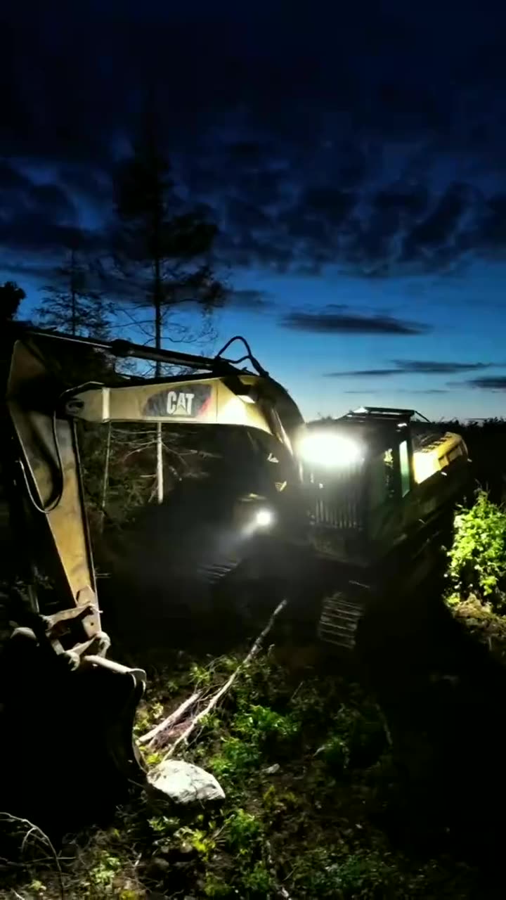 Pelle mécanique éclairée par ses phares en forêt